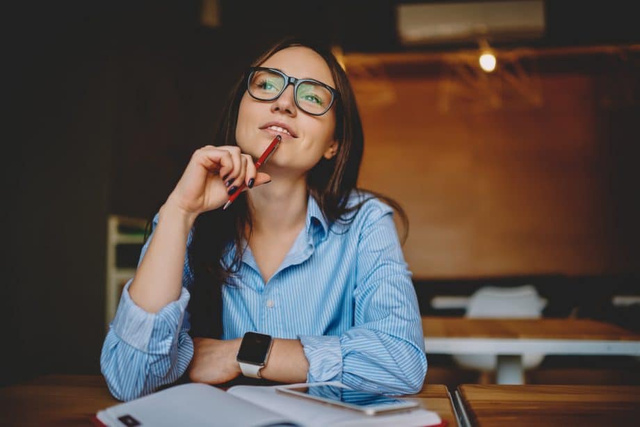 Professional woman in a coffee shop setting looking up appearing to be thinking about something intently.