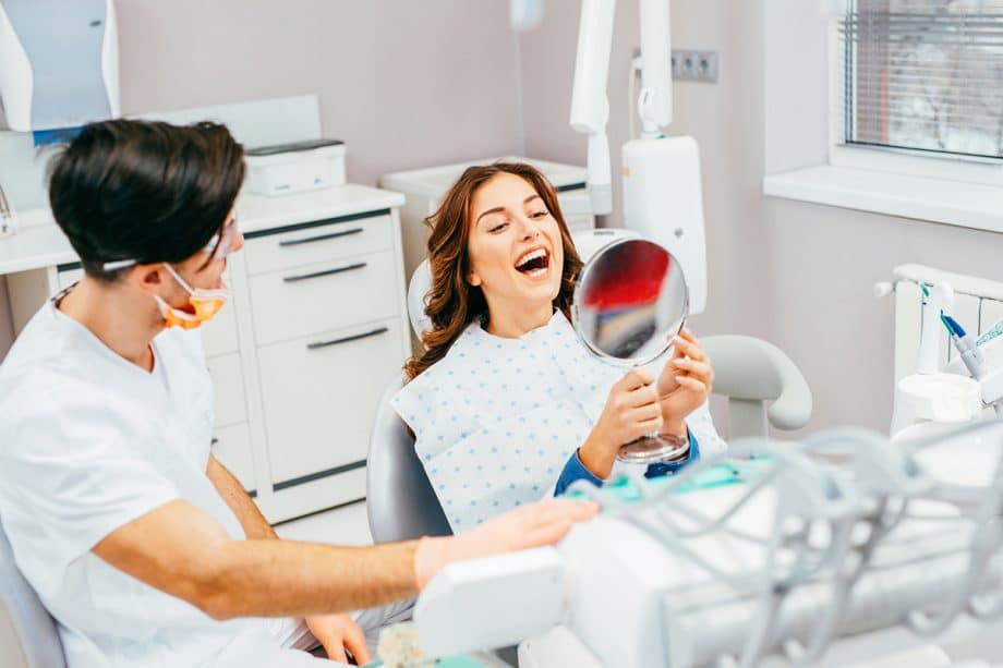 woman in dental chair looking at her teeth in the mirror