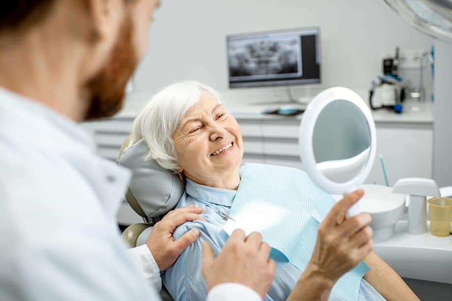 older woman in dental chair looking at her smile in the mirror